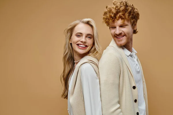 Joyous young models in light-colored vintage attire standing back to back on beige backdrop — Stock Photo