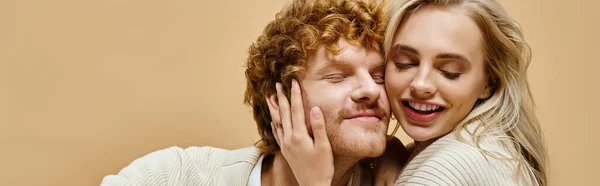 Overjoyed blonde woman with closed eyes embracing head of trendy redhead man on beige, banner — Stock Photo