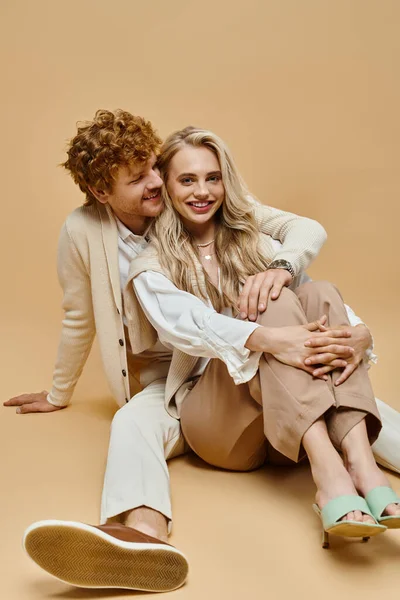 Feliz ruiva homem abraçando elegante mulher loira no chão no fundo bege, velho estilo dinheiro — Fotografia de Stock