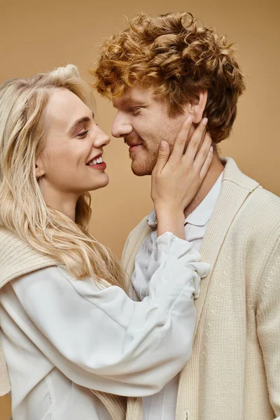 Smiling blonde woman hugging face of young redhead man on beige backdrop, old money style concept — Stock Photo