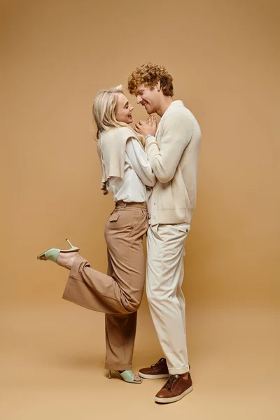 Comprimento total do casal em roupas elegantes de cor clara de mãos dadas e rindo em pano de fundo bege — Fotografia de Stock
