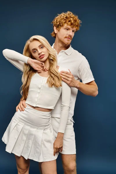 Sensual blonde woman in white trendy clothes posing near young redhead man on blue, classic fashion — Stock Photo
