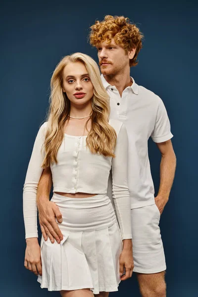 Attractive blonde woman in white clothes looking at camera near redhead aristocratic man on blue — Stock Photo