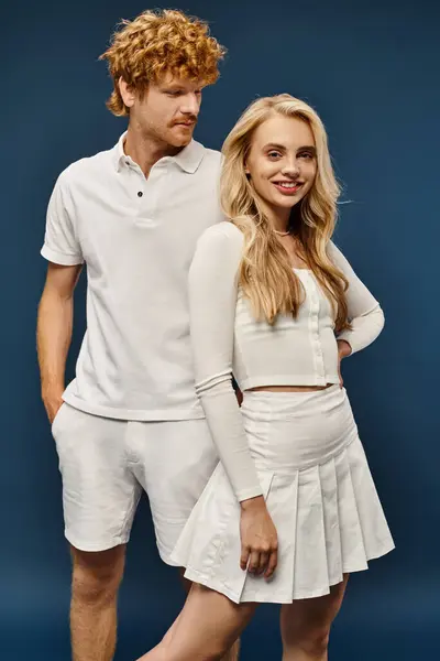 Charming blonde woman in white trendy outfit smiling at camera near handsome redhead man on blue — Stock Photo