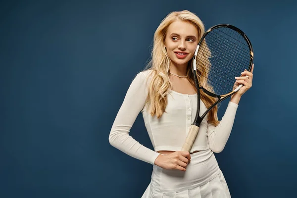 Положительный спортивная блондинка модель в белом наряде проведение теннисной ракетки и глядя в сторону на синий — стоковое фото