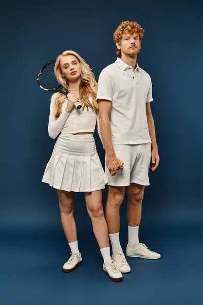 Full length of blonde woman with tennis racquet near trendy redhead man in white clothes on blue — Stock Photo