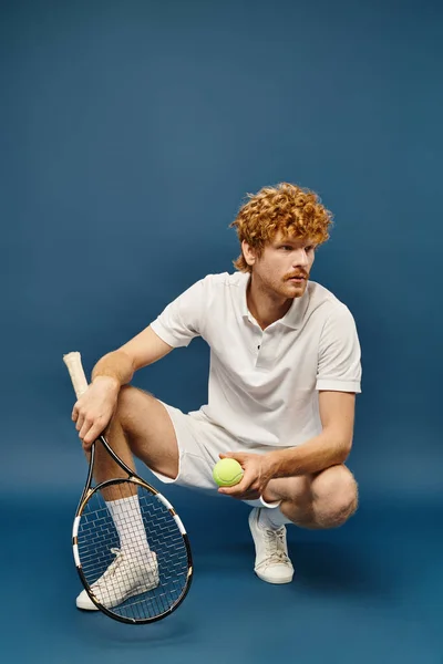 Стильний чоловік у білому одязі з тенісним ракеткою і м'ячем, що сидить на гастролях, дивлячись на синій — стокове фото