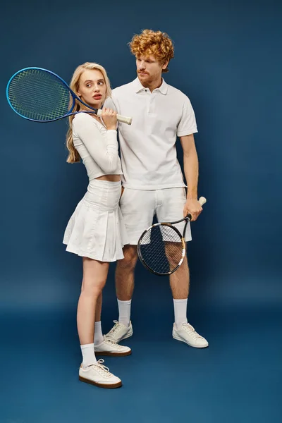 Повна довжина рудого чоловіка, дивлячись на блондинку з тенісним ракеткою, дивиться на синій — стокове фото