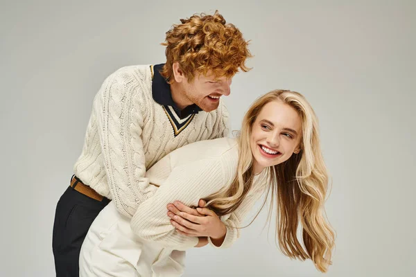 Cheerful redhead man hugging excited blonde woman and having fun on grey backdrop, classic fashion — Stock Photo