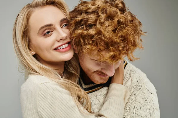 Feliz e elegante mulher loira abraçando jovem ruiva homem no cinza, relacionamento casal na moda — Fotografia de Stock
