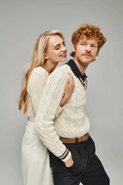 Freudige blonde Frau umarmt jungen rothaarigen Mann in trendiger Freizeitkleidung auf grauer, zeitloser Mode — Stockfoto