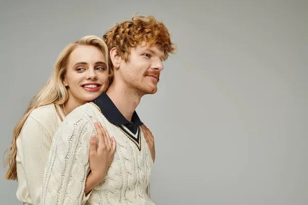 Jolly blonde woman embracing young redhead man in stylish casual clothes on grey, timeless fashion — Stock Photo