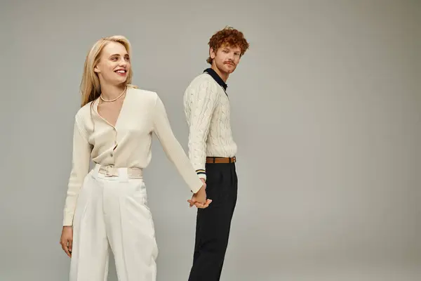 Щаслива блондинка і рудий чоловік в модному повсякденному одязі тримає руки на сірому, старому стилі моди — стокове фото