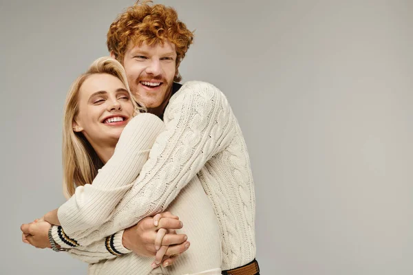 Excited redhead man embracing blonde woman in trendy casual clothes on grey, timeless fashion — Stock Photo