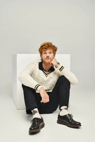 Pensive dreamy man in casual clothes looking at camera sitting near white cube on grey backdrop — Stock Photo