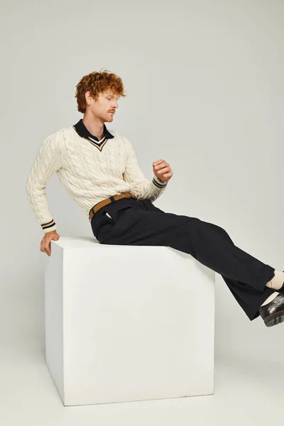 Giovane uomo rossa in abiti alla moda seduto su cubo bianco su grigio, vecchio concetto di stile soldi — Foto stock