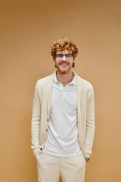 Homme rousse heureux dans les lunettes et les vêtements légers avec les mains dans les poches regardant caméra sur beige — Photo de stock