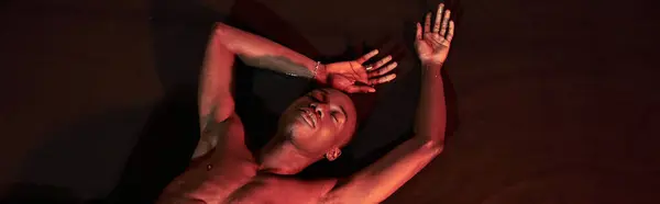 Sexy homme afro-américain couché seins nus sur l'eau avec les yeux fermés, lumières sombres, concept de mode — Photo de stock