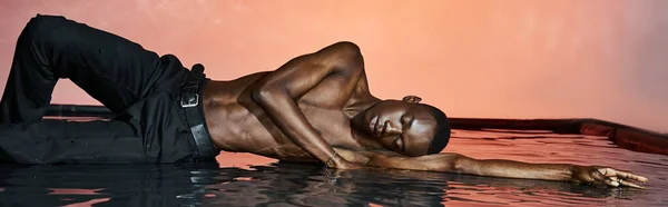 Atractivo hombre afroamericano en pantalones mojados acostado en la superficie del agua con los ojos cerrados, luces, pancarta - foto de stock