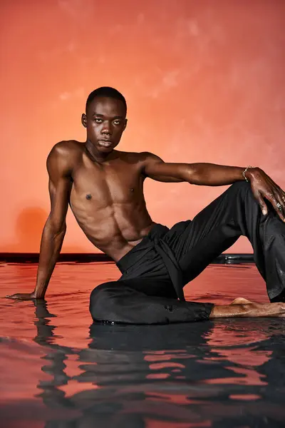Handsome african american man sitting topless on water surface and looking at camera, lights — Stock Photo