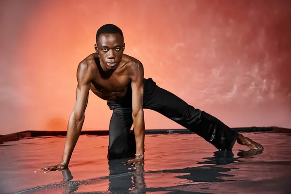 Atractivo afroamericano hombre sentado en topless en la superficie del agua y mirando a la cámara, luces - foto de stock