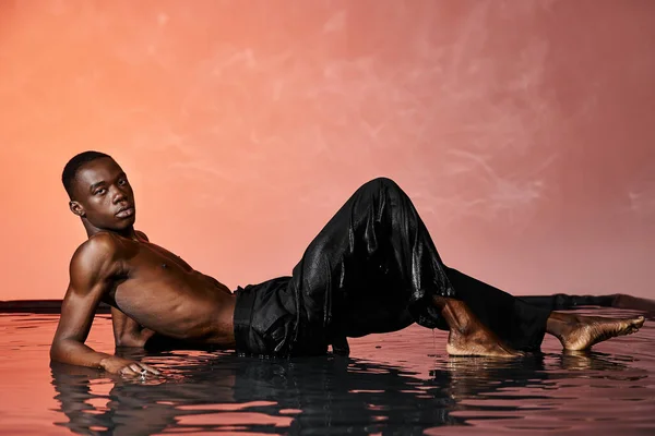 Attractive african american man reclining topless on water surface and looking at camera, red lights — Stock Photo