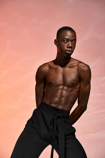 Sexy african american man standing topless in black pants surrounded by lights and looking away — Stock Photo