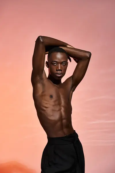 Accattivante uomo afroamericano senza maglietta in piedi e guardando la fotocamera circondata da luci rosse — Foto stock