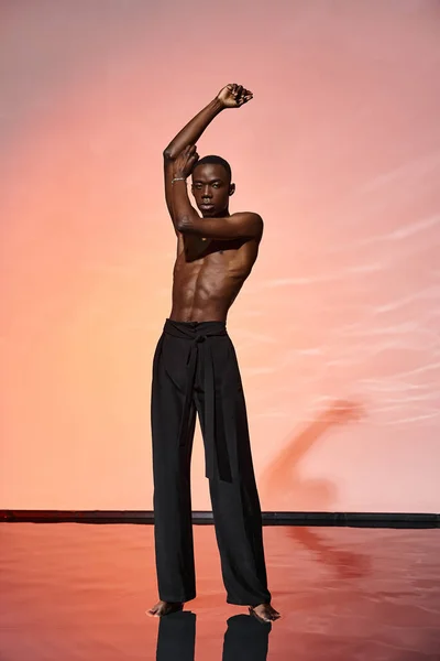 Attrayant sans chemise homme afro-américain debout et regardant la caméra entourée de lumières rouges — Photo de stock