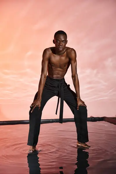 Alluring shirtless african american man standing and looking at camera surrounded by red lights — Stock Photo