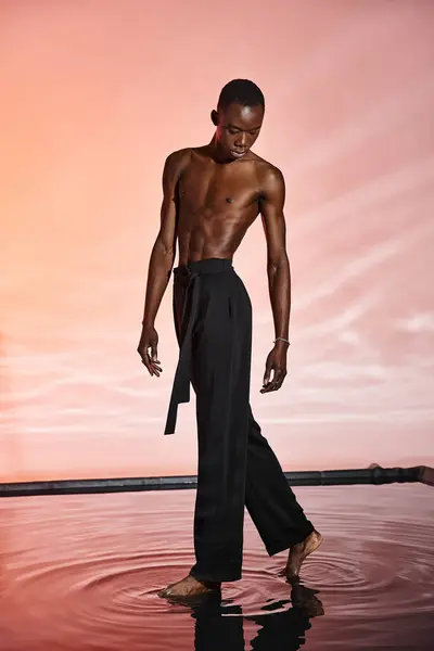 Bell'aspetto uomo afroamericano senza maglietta che indossa pantaloni neri eleganti circondati da luci rosse — Foto stock