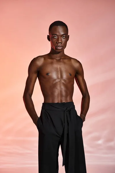 Alluring shirtless african american man standing and looking at camera surrounded by red lights — Stock Photo