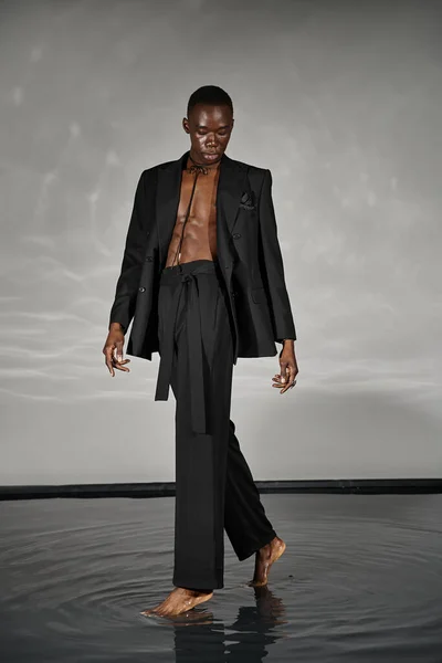 Charming stylish african american man in sexy unbuttoned suit posing on gray watery background — Stock Photo