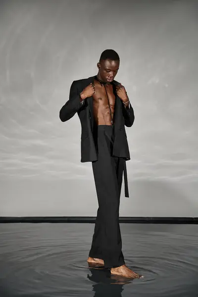 Charming stylish african american man in sexy unbuttoned suit posing on gray watery background — Stock Photo