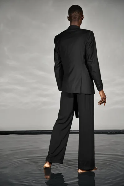 Back view of young african american man in black elegant suit posing on gray watery backdrop — Stock Photo