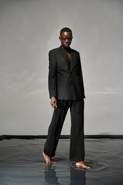 Handsome stylish african american man in sexy unbuttoned suit posing on gray watery background — Stock Photo