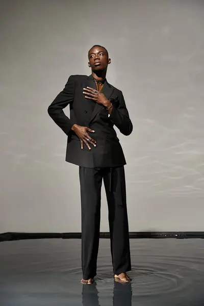 Tentador hombre afroamericano con estilo en traje desabotonado sexy posando sobre fondo acuoso gris - foto de stock