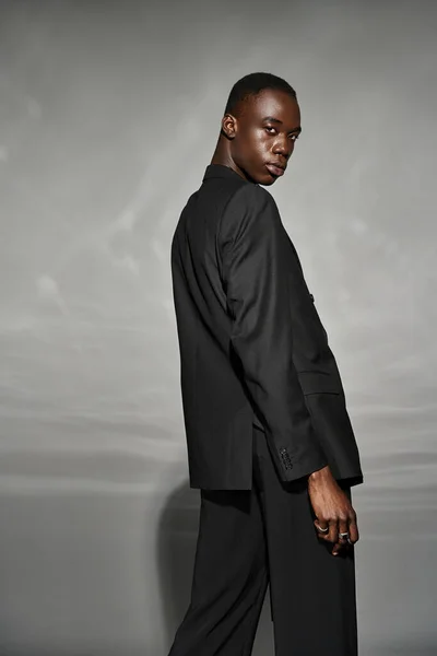 Engaging african american man in unbuttoned black suit posing alluringly and looking at camera — Stock Photo