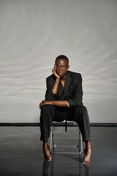 Appealing african american man in sexy unbuttoned suit sitting on chair and looking at camera — Stock Photo