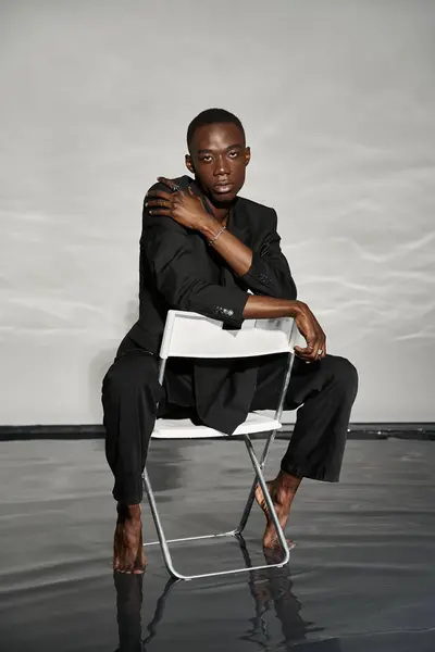 Appealing sexy african american man in elegant black suit sitting on chair and looking at camera — Stock Photo