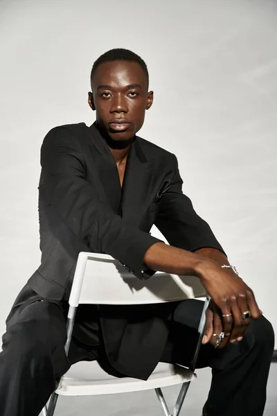 Handsome sexy african american man in elegant black suit sitting on chair and looking at camera — Stock Photo