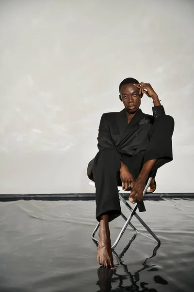 Stylish sexy african american man in elegant black suit sitting on chair and looking at camera — Stock Photo