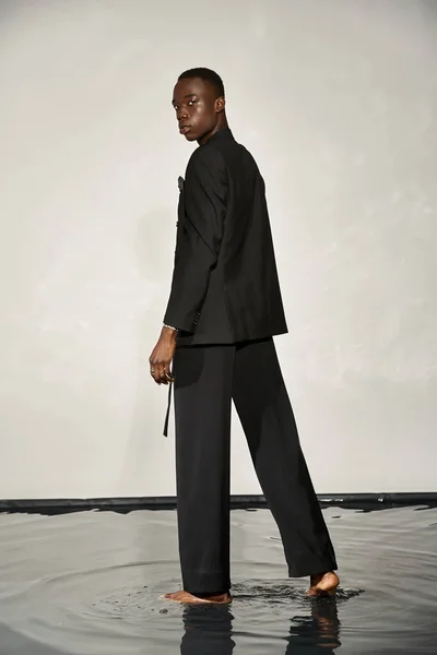 Appealing african american man in black sexy suit posing attractively on gray watery background — Stock Photo