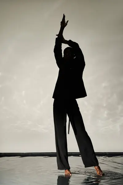 Silhouette of stylish african american man posing barefoot in suit on watery backdrop in shadows — Stock Photo