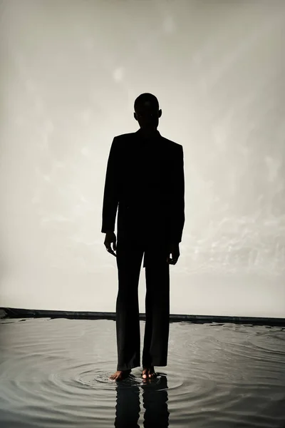 Silhouette of tempting african american man posing barefoot in suit on watery backdrop in shadows — Stock Photo