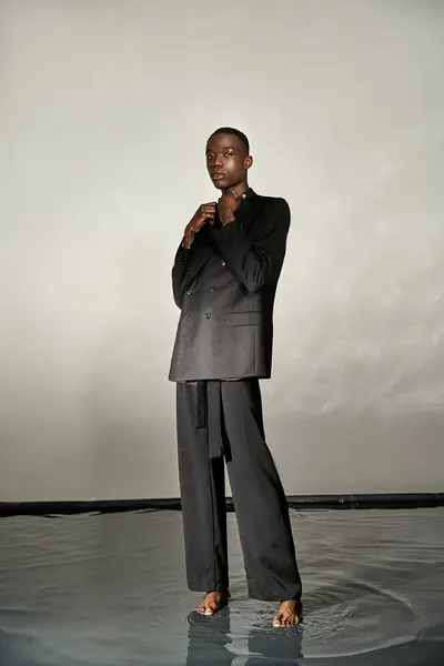 Bonito afro americano homem no preto sexy terno posando atrativamente no cinza aguado fundo — Fotografia de Stock