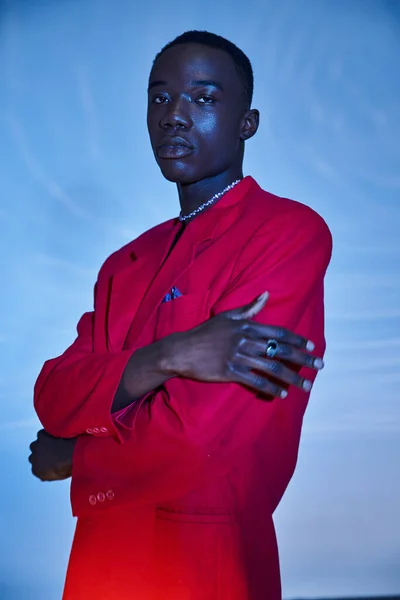 Привлекательный молодой африканский американец в красном ярком пиджаке позирует на голубом водянистом фоне — стоковое фото