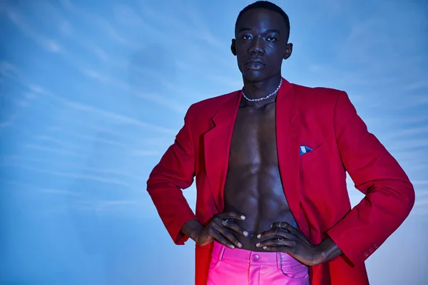 Attrayant jeune homme afro-américain en rouge vibrant blazer posant sur fond bleu aqueux — Photo de stock