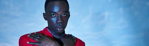 Trendy african american man in red vibrant blazer posing on blue watery background, banner — Stock Photo