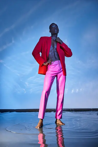 Enticing stylish african american man in pink pants and red blazer posing on blue watery backdrop — Stock Photo